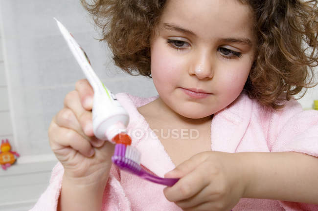 Маленькая девочка прижимает зубную пасту к зубной щетке — стоковое фото