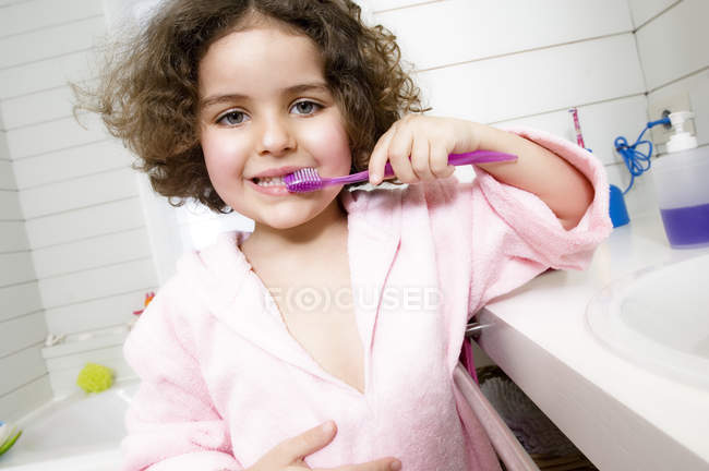 Little girl brushing teeth in bathroom and looking at camera — Stock Photo