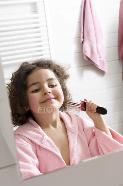 Petite fille dans la salle de bain brossant les cheveux devant le miroir — Photo de stock