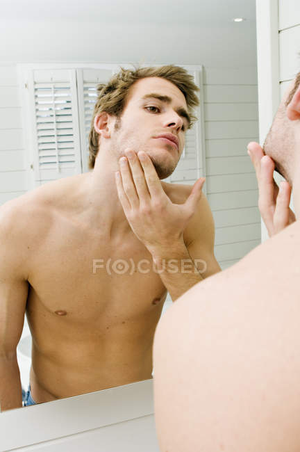 Shirtless man looking at bathroom mirror — Stock Photo