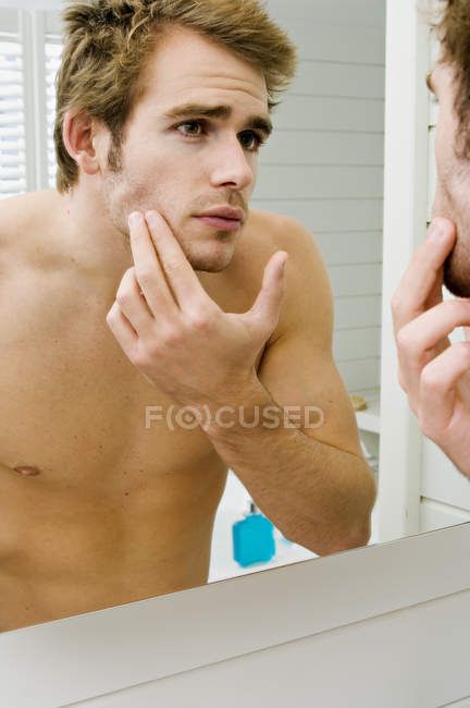 Shirtless giovane uomo controllando il viso davanti allo specchio del bagno — Foto stock