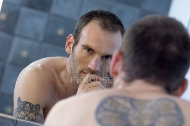 Tattooed shirtless man standing in front of bathroom mirror — Stock Photo