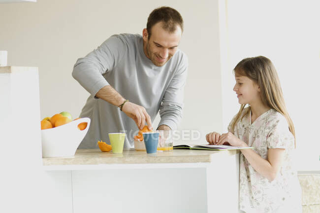 Маленькая девочка смотрит, как мужчина сжимает апельсины на кухне — стоковое фото