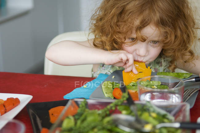 Little ginger girl eating with hands at lunch table — Stock Photo