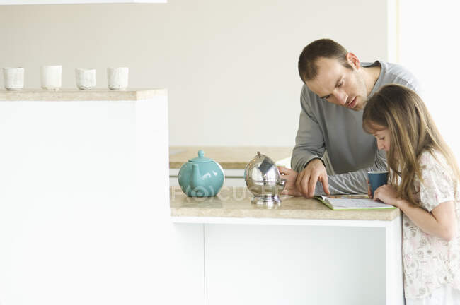 Mann und kleines Mädchen stehen in der Küche und lesen Schulheft — Stockfoto