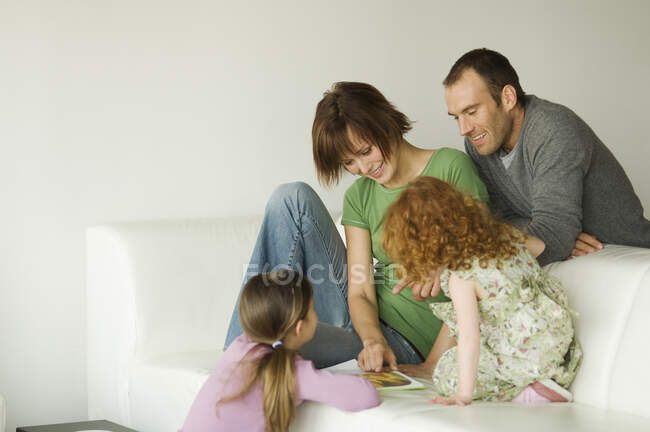 Пара и две маленькие девочки читают журнал в гостиной — стоковое фото