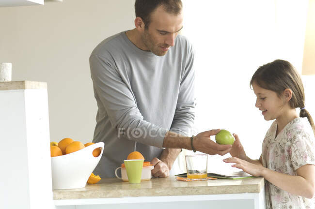 Uomo in piedi in cucina, dando una mela alla bambina — Foto stock