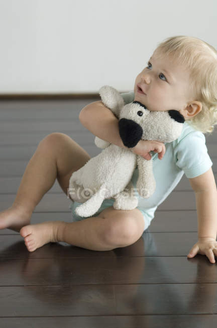 Маленький мальчик сидит на полу и держит плюшевую собаку — стоковое фото