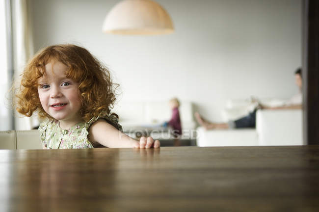 Retrato de linda niña de jengibre sentado en la mesa - foto de stock