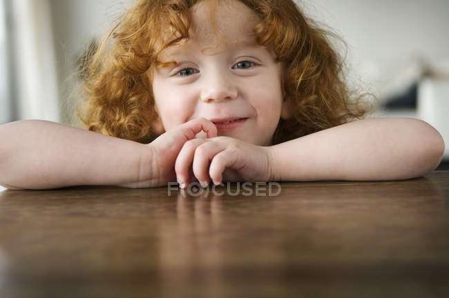 Портрет милой рыжей девочки, сидящей за столом — стоковое фото