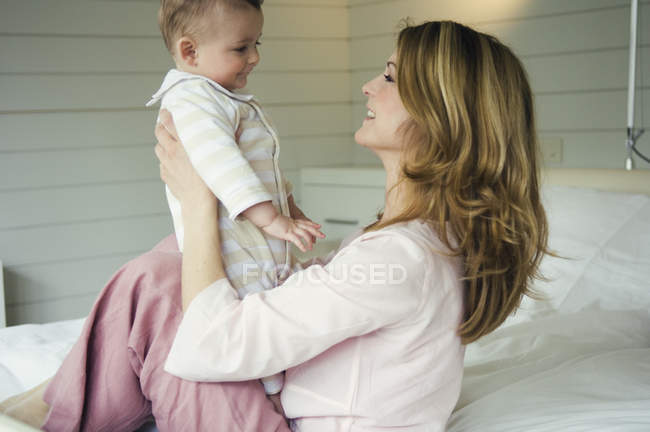 Frau hält Baby auf Bett und schaut einander an — Stockfoto