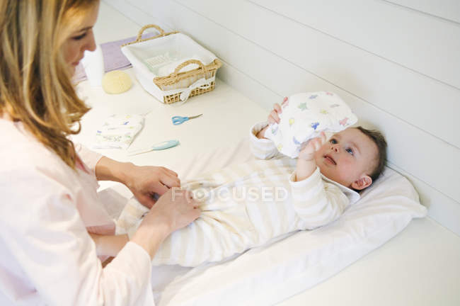 Frau zieht Baby Junge aus, der auf Bett liegt — Stockfoto