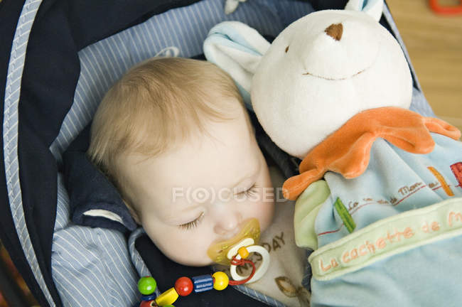Baby girl sleeping in baby carrier with stuffed toy — Stock Photo