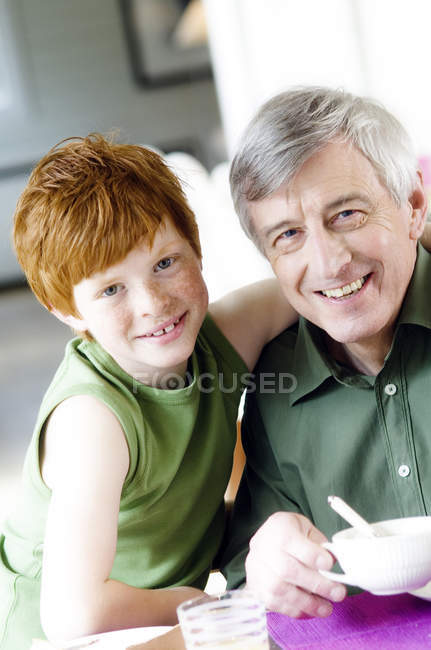 Niño abrazando sonriente hombre mayor, mirando a la cámara - foto de stock