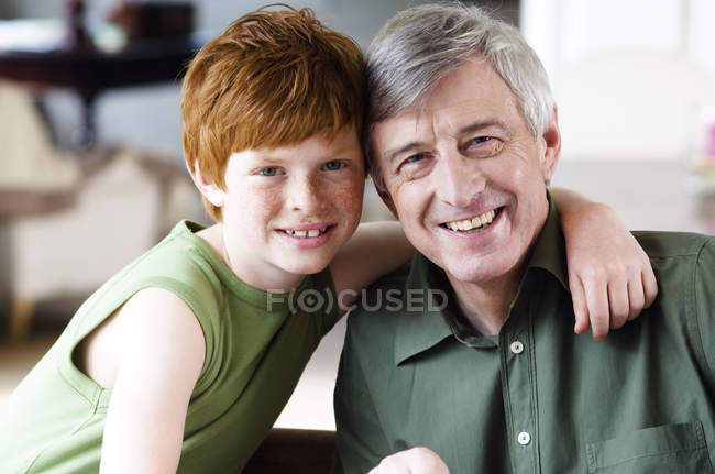Niño abrazando sonriente hombre mayor, mirando a la cámara - foto de stock