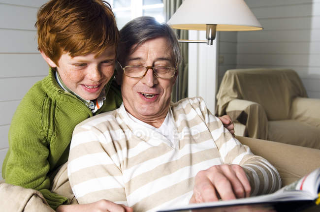 Старший мужчина и мальчик читают книгу дома — стоковое фото