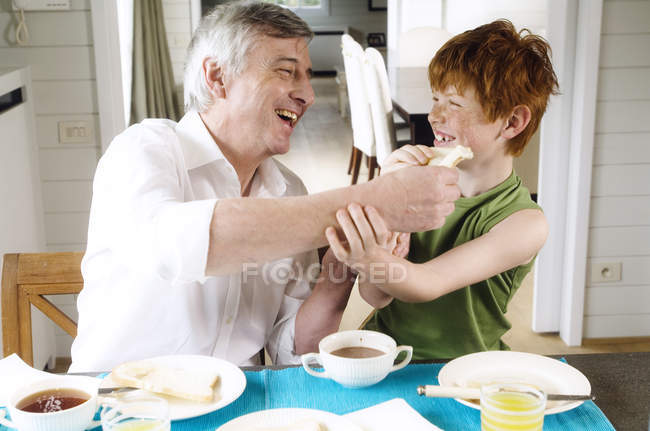 Smiling senior man and boy having breakfast at home — Stock Photo
