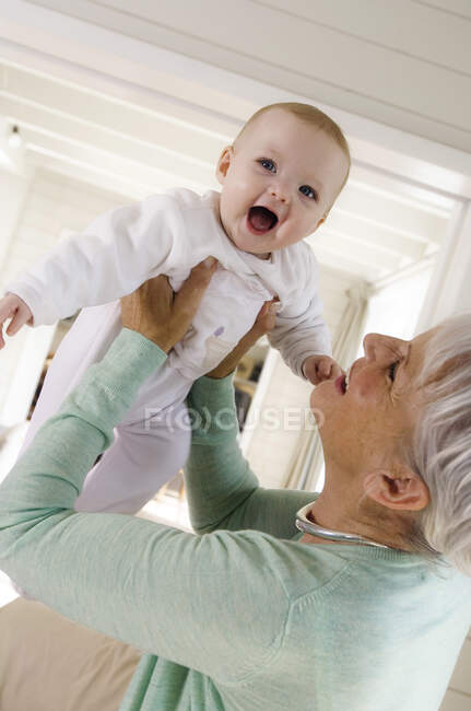Femme âgée soulevant bébé fille dans l'air — Photo de stock