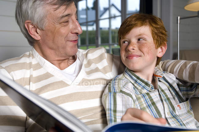 Hombre mayor con libro y niño mirándose - foto de stock