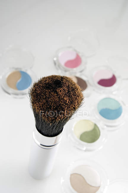 Primer plano de las cajas de sombra de ojos y el cepillo de maquillaje sobre fondo blanco - foto de stock
