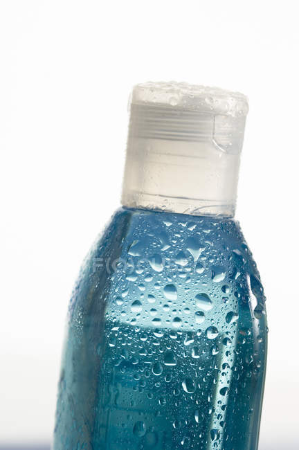 Gros plan de bouteille en plastique bleu avec des gouttes d'eau sur fond blanc — Photo de stock