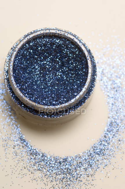 Primer plano de lentejuelas azul oscuro en frasco sobre fondo beige - foto de stock