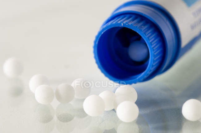 Primer plano del tubo de plástico de píldoras homeopáticas sobre fondo blanco - foto de stock