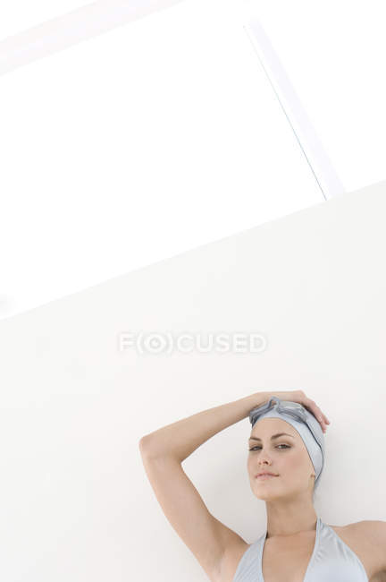 Portrait of young woman in bikini, swimming cap and goggles leaning on wall — Stock Photo