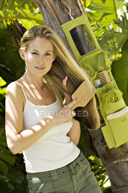 Junge Frau bürstet Haare im Freien und schaut in die Kamera — Stockfoto
