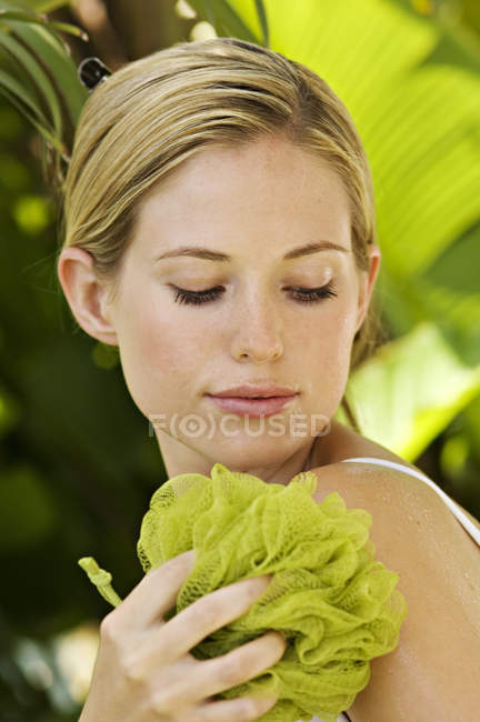 Portrait of young woman cleaning shoulder with mesh sponge outdoors — Stock Photo