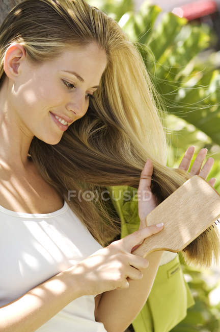 Портрет усміхненої молодої жінки чистить волосся на відкритому повітрі — стокове фото