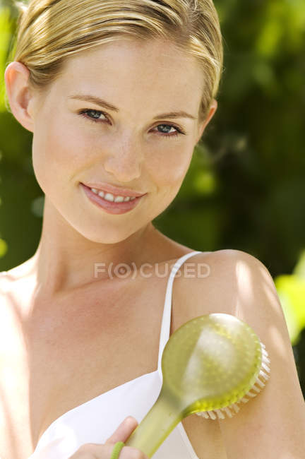 Ritratto di giovane donna sorridente e spazzolante spalla all'aperto — Foto stock