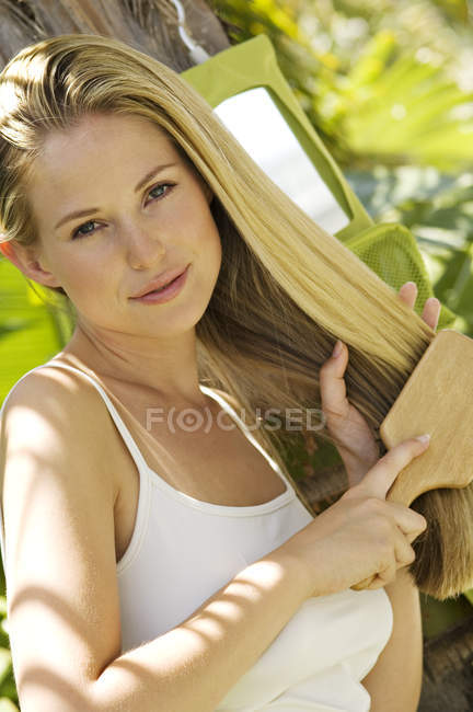 Portrait of young blond woman brushing hair outdoors — Stock Photo