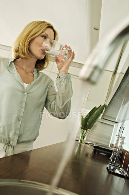 Mulher bebendo água da torneira de vidro na cozinha — Fotografia de Stock