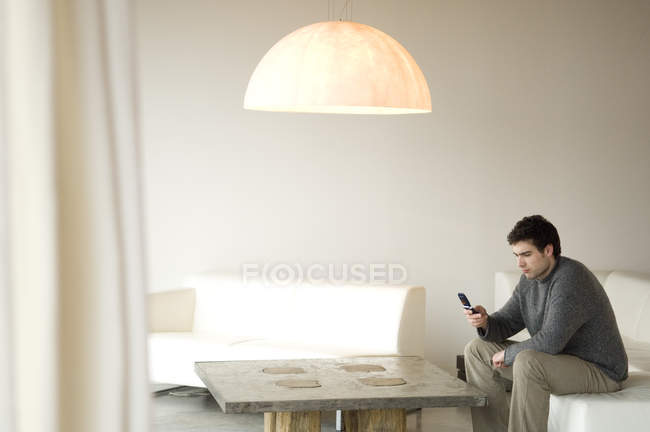 Mann sitzt auf Sofa im Wohnzimmer und benutzt Handy — Stockfoto