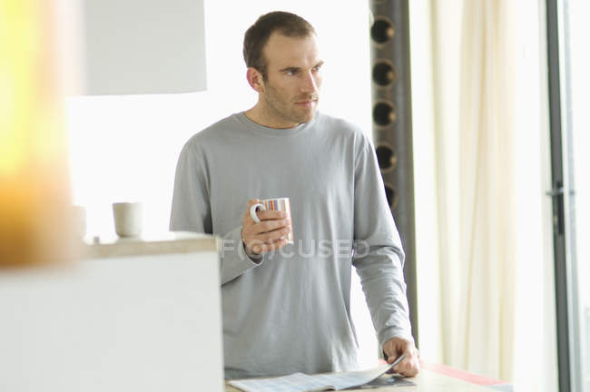 Homme réfléchi debout dans la cuisine et tenant tasse — Photo de stock