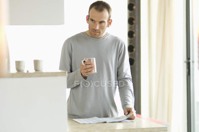 Продуманий чоловік стоїть на кухні і тримає кухоль — стокове фото