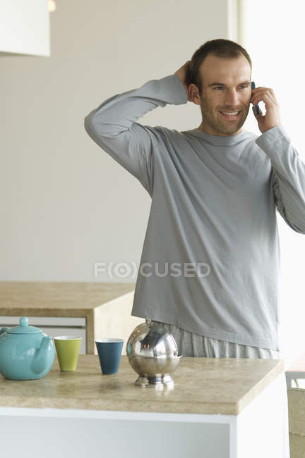 Homem de pé na cozinha, falando no celular — Fotografia de Stock