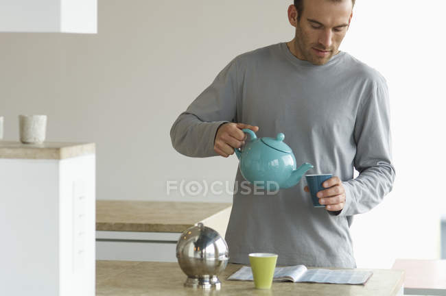 Homem de pé na cozinha, derramando chá em xícara — Fotografia de Stock
