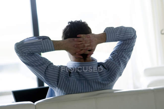 Visão traseira do homem descansando no sofá com as mãos atrás da cabeça — Fotografia de Stock