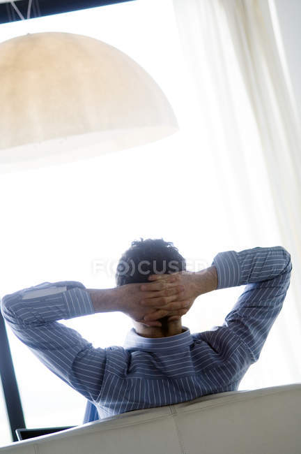 Vista trasera del hombre descansando en el sofá con las manos detrás de la cabeza - foto de stock