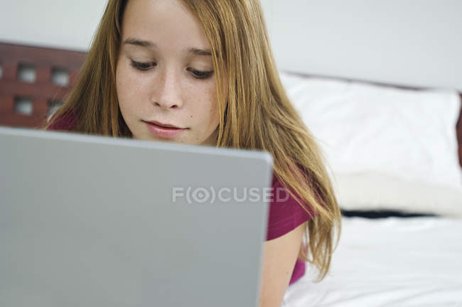 Дівчина-підліток, що використовує ноутбук, лежить на ліжку — стокове фото