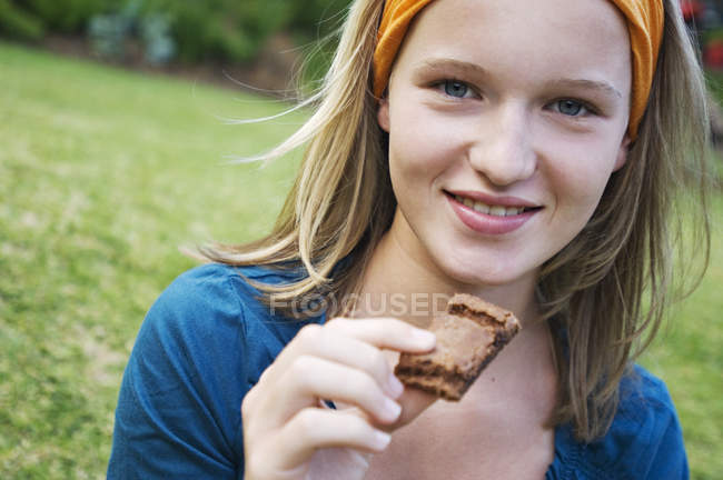 Retrato de una adolescente sonriente sosteniendo un pedazo de pastel al aire libre - foto de stock