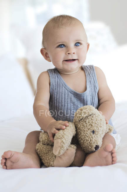 Baby boy sitting on bed with teddy bear — Stock Photo