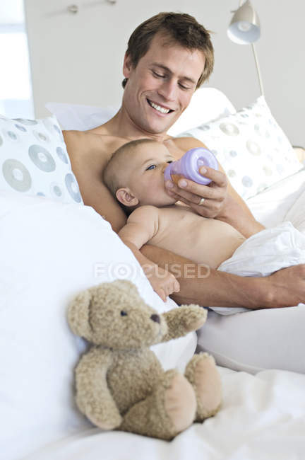 Sorrindo pai alimentando bebê menino na cama — Fotografia de Stock