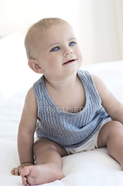 Cute baby boy with blue eyes sitting on bed — daytime, indoors - Stock  Photo | #222871016