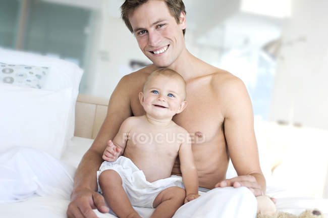 Портрет счастливого отца и мальчика, сидящего на кровати — стоковое фото