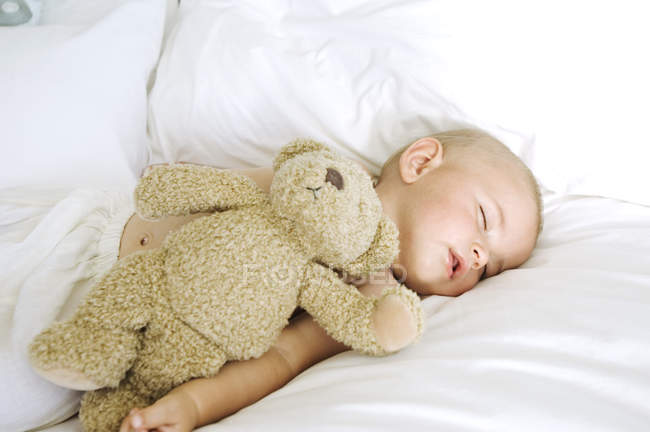 Cute baby sleeping on bed with stuffed toy — Stock Photo