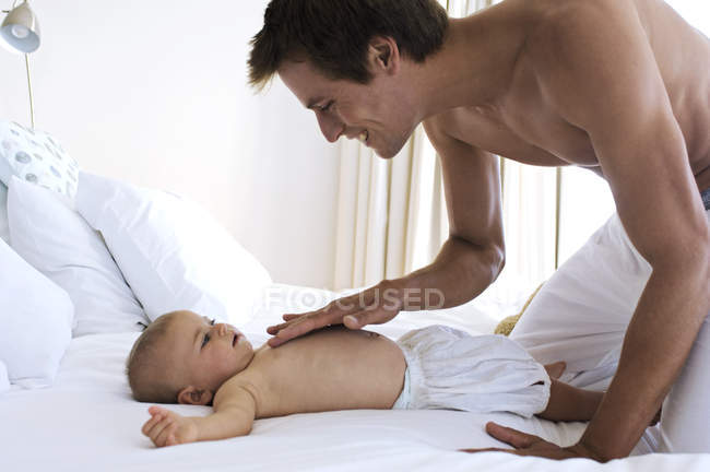 Father touching baby boy chest in bed — Stock Photo
