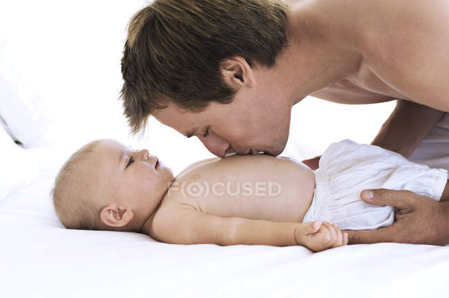 Ritratto di padre che bacia il petto del bambino sul letto — Foto stock